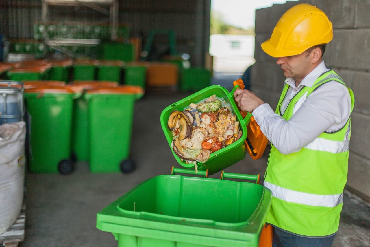 man in a yellow hard hat and high vis vest emptying food waste into a recycling bin