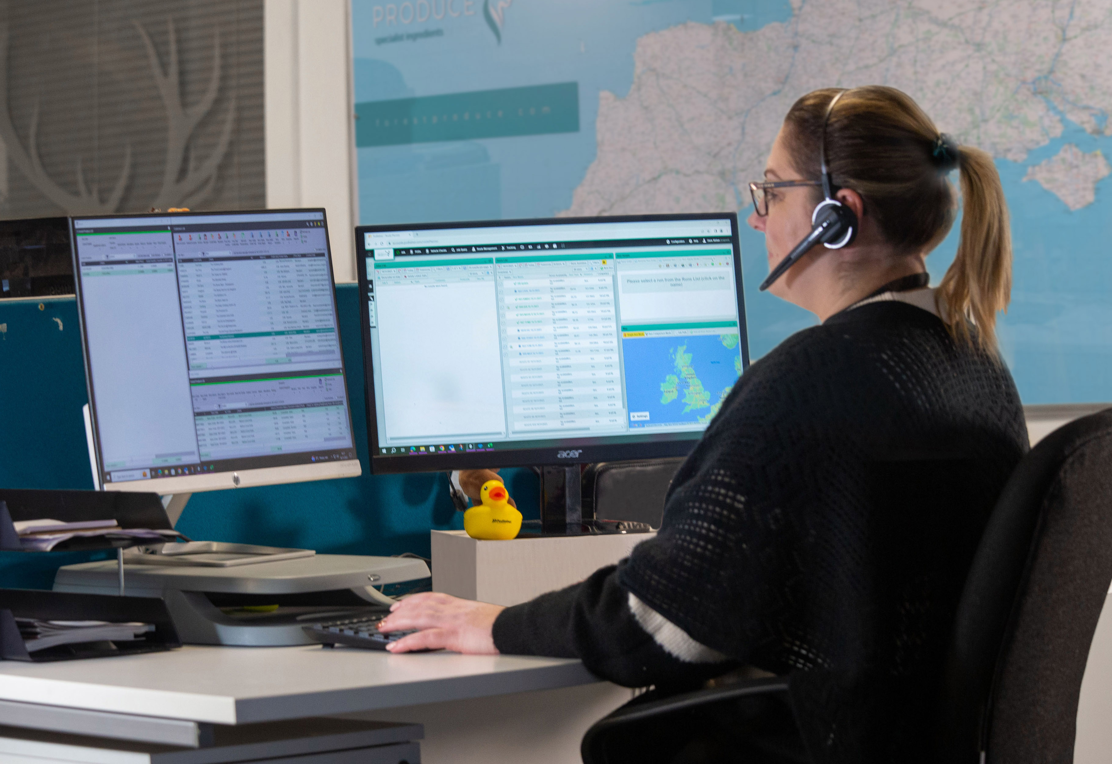 lady sitting at a computer with two screens with a headset on