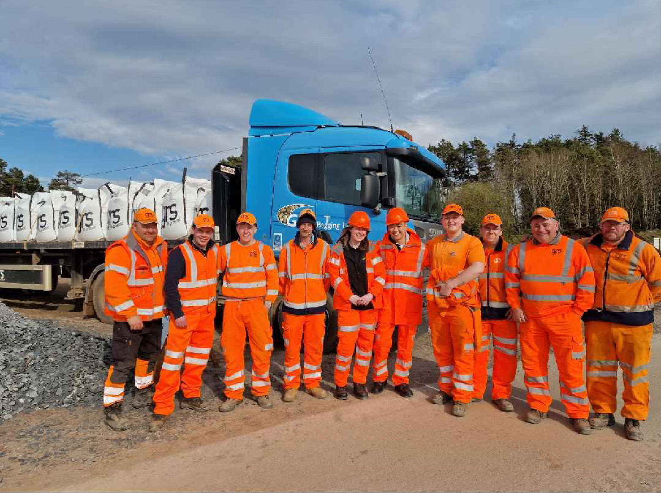 Group of people in orange high vis PPE standing infront of a lorry.