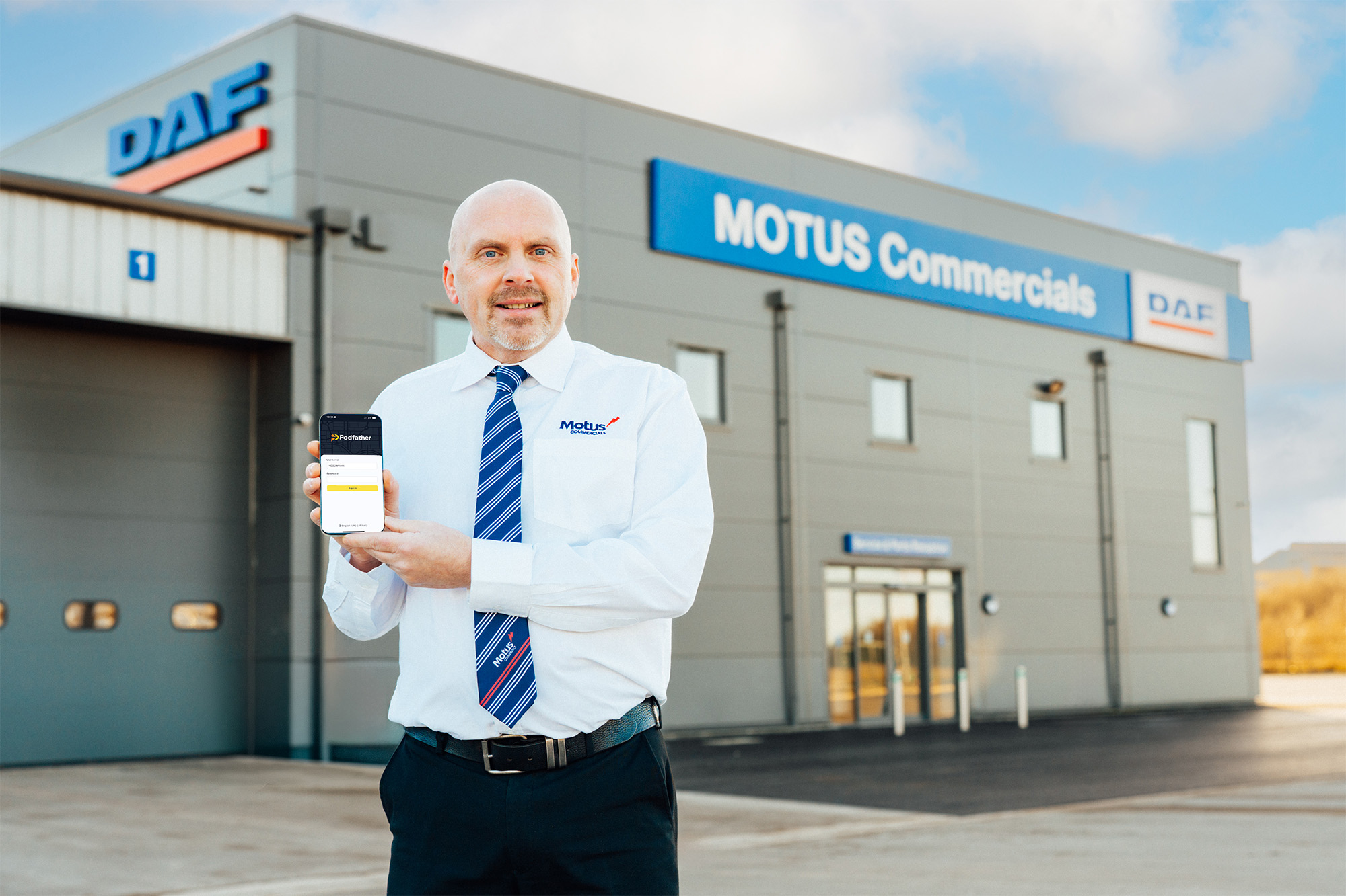 Motus employee standing infront of building holding a device with Podfather login screen