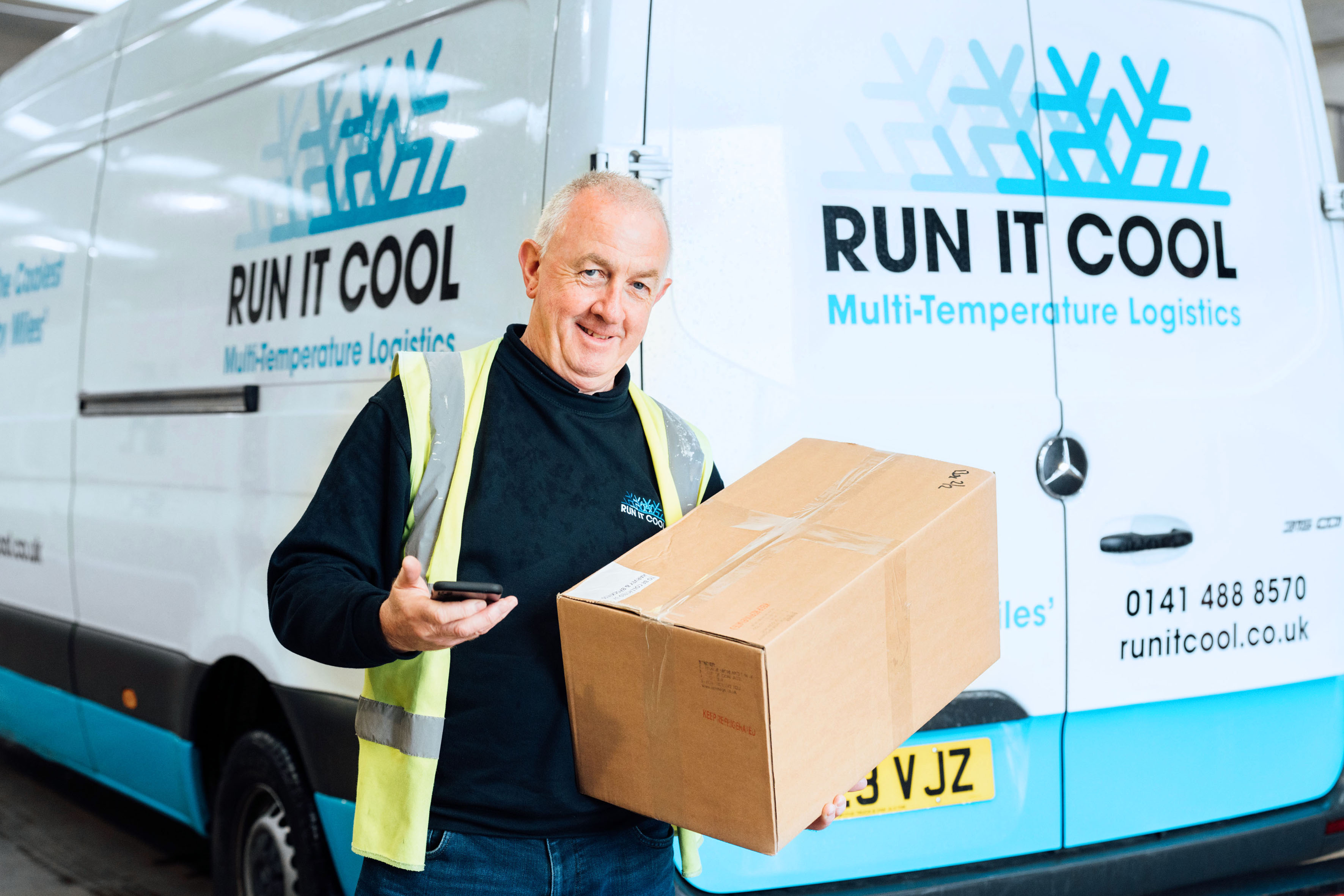 Man standing in front of a van holding a smartphone and a large box