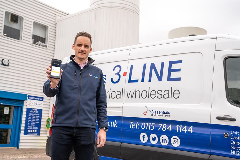 A man in a navy jacket standing in front of a blue and while van; he's holding a mobile phone
