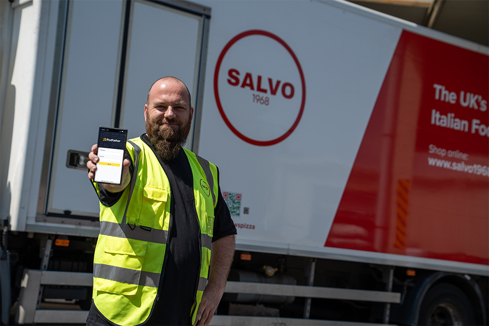 Man with a beard standing in front of a Salvo branded truck wearing a high vis vest and holding a mobile phone