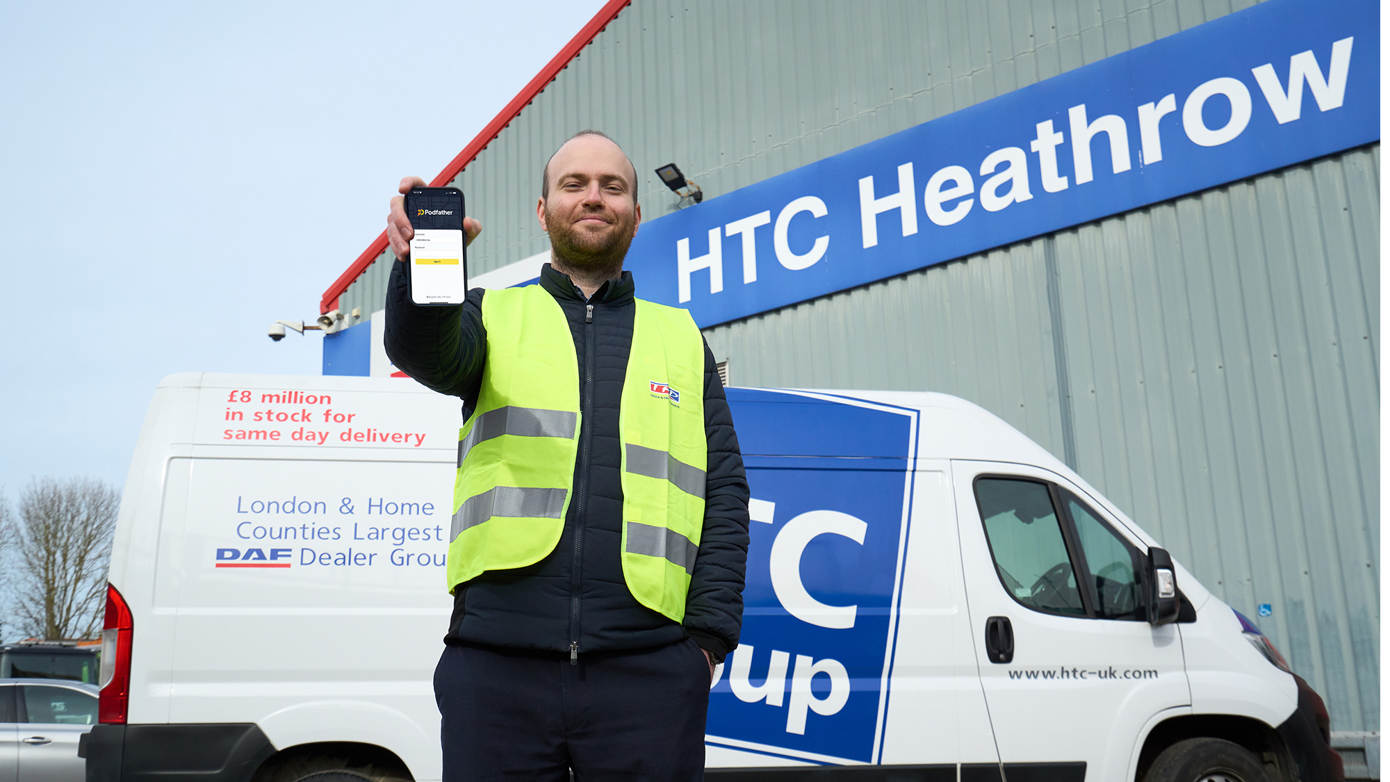 Man in high vis standing in front of a white van outside the HTC Heathrow building