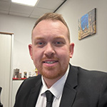 Man in a dark suit and tie smiling at the camera