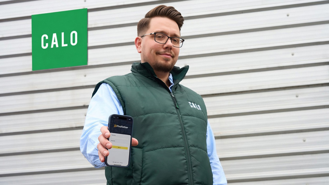 Man holding a mobile device standing in front of a building with a Calo sign