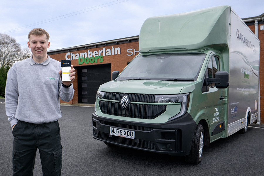 Smiling man  holding a mobile device standing infront of a green van and a depot