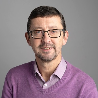 Man wearing glasses and a purple jumper smiling at the camera