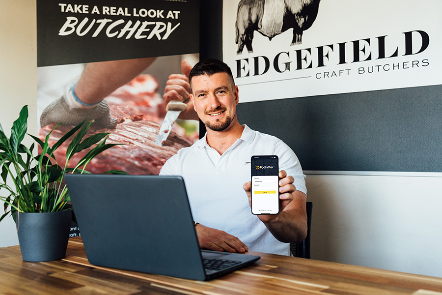 Smiling man sitting at a laptop holding a mobile device