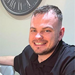 Man smiling at the camera with a clock in the background