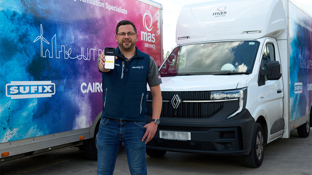 MAS employee holding a mobile device standing in front of 2 vans