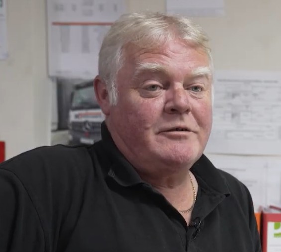 Man in a black polo shirt sitting in a transport office