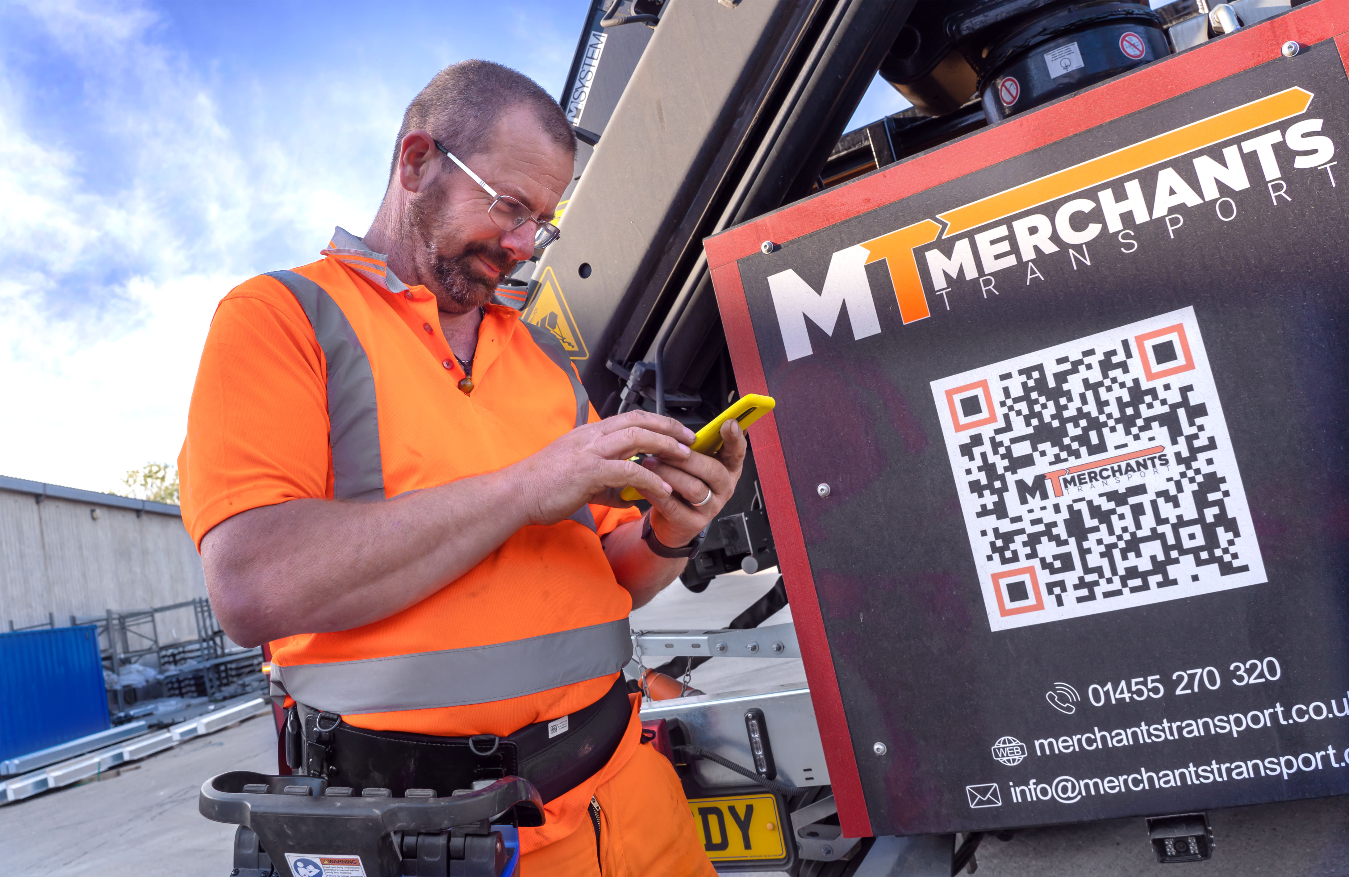 Man in an orange high vis outfit standing by a truck looking down at a mobile phone