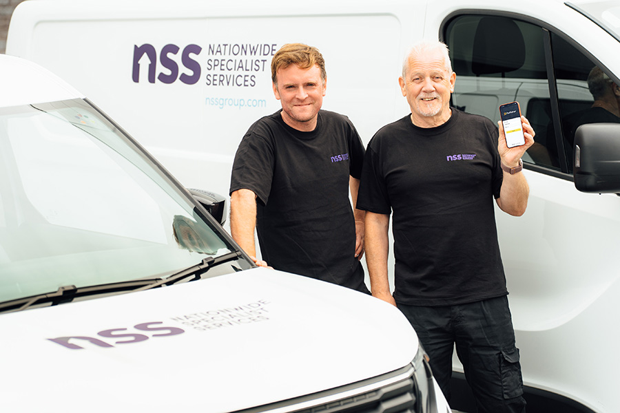 Two men standing in front of two vans; one is holding a mobile device
