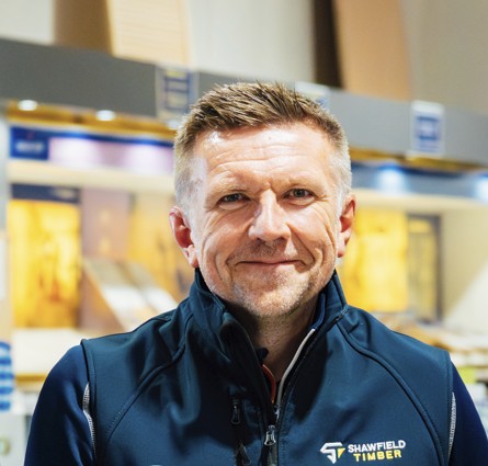 Smiling man wearing a blue jacket standing in a warehouse