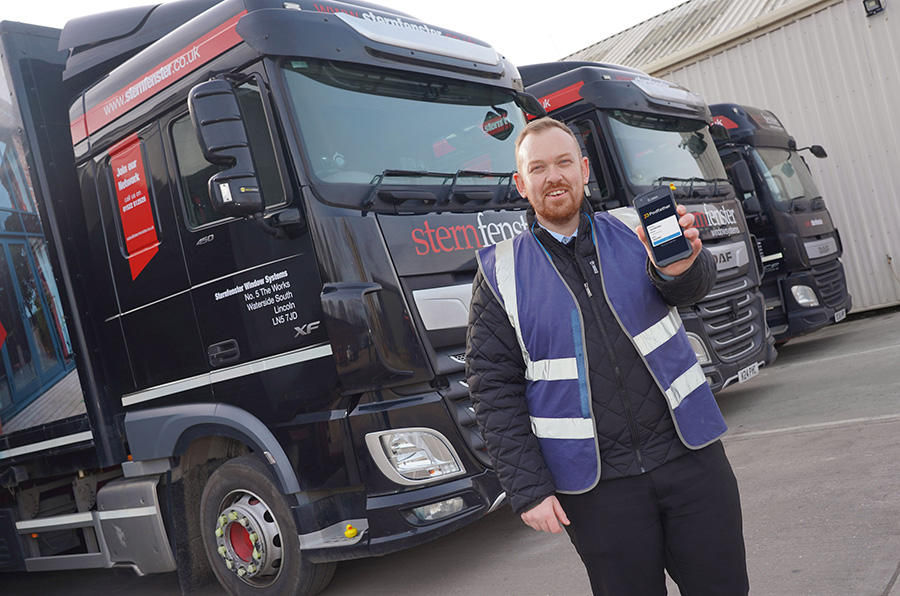 Man in a high vis holding a phone standing in front of 3 trucks