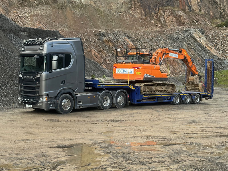 Silver HGV with an orange digger on the back