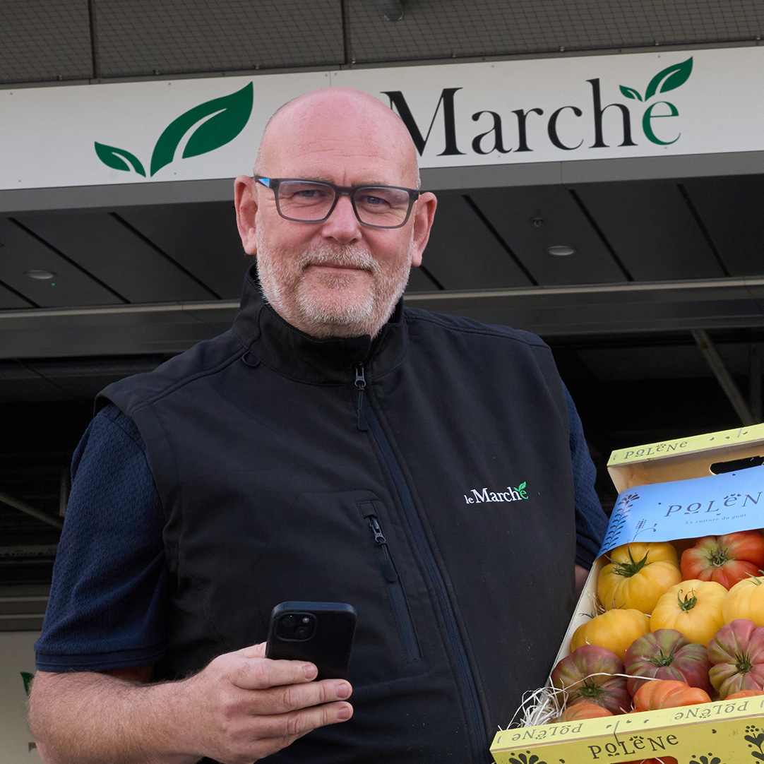 Man holding tomatoes and a mobile device looking at the camera