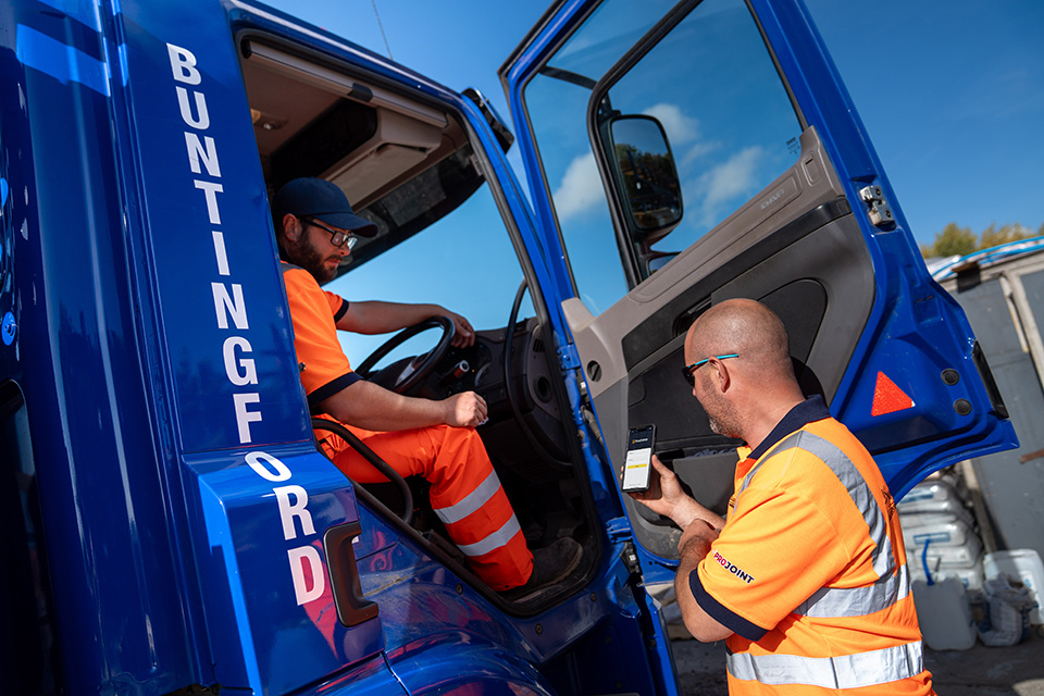 Two men looking at a mobile device, one is sitting in the cab of a blue truck