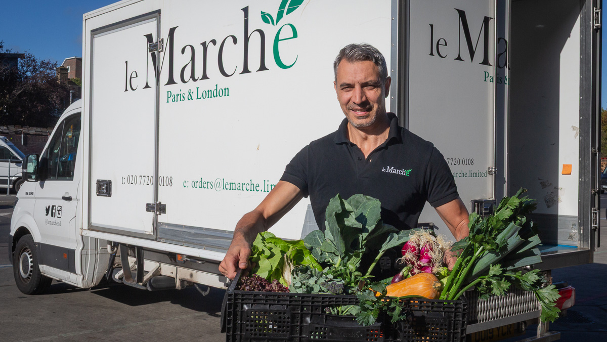 Smiling man holding a box of mixed vegetables standing in front of a van